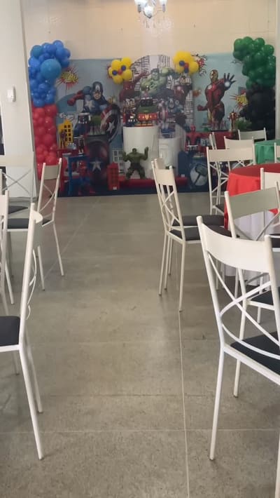 Corredor entre as mesas montadas, com cadeiras brancas e painel temático ao fundo