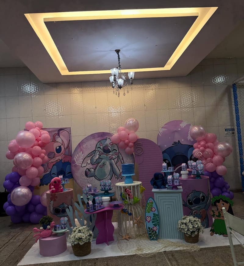 Painel do Lilo & Stitch em lilás e rosa, com arco de balões e mesa de doces