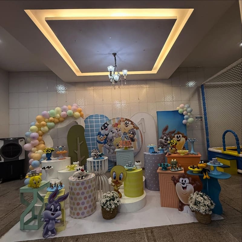 Cenário Baby Looney Tunes em tons pastel, com arco de balões e personagens na mesa