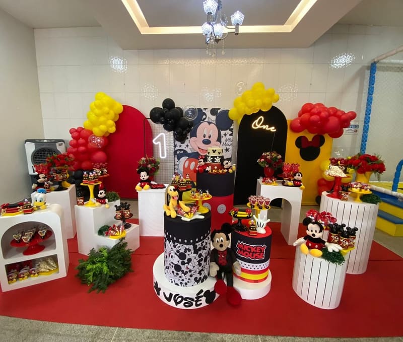Decoração do Mickey com painel vermelho e preto, balões e mesa do bolo sobre tapete vermelho