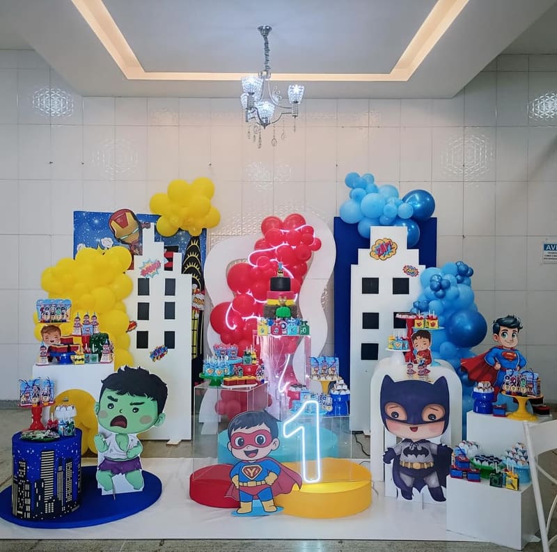 Cenário de super-heróis com prédios recortados, balões azuis e vermelhos e bonecos na mesa